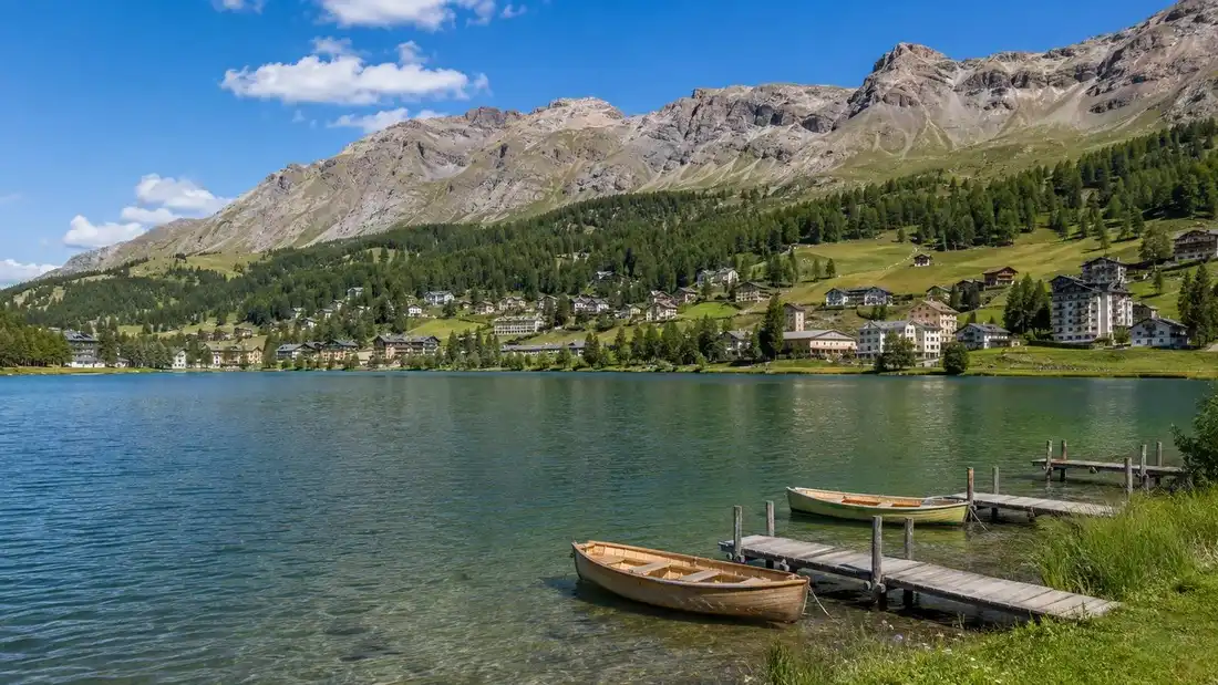 Jezero v sirokem vysokohorskem udoli u Davosu s drevenymi moly a mestem na svahu