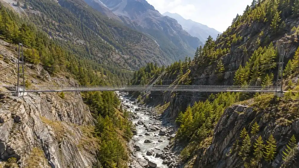 Ocelovy visuty most nad hlubokou skalni roklinou s bystrinou u Saas-Fee