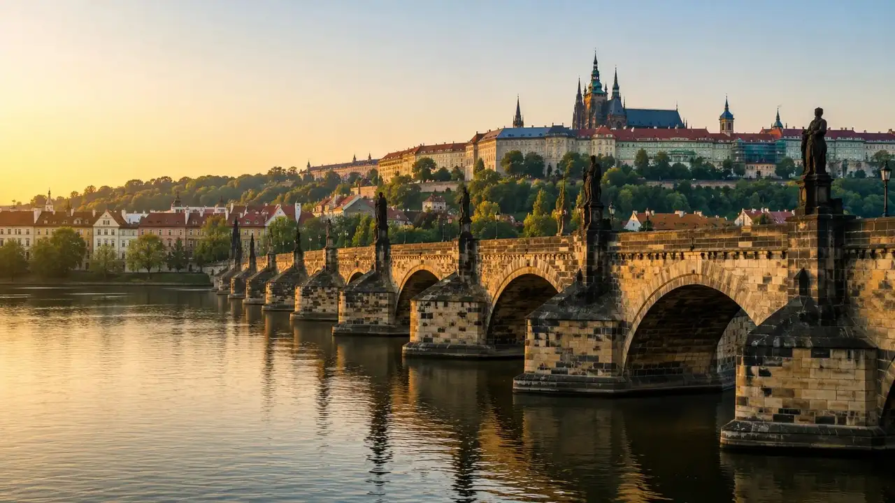 Kamenný most se sochami přes řeku a hradní panorama s katedrálou za svítání