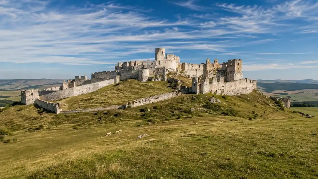 Rozlehlá zřícenina hradu na travnatém vápencovém kopci nad rovinou